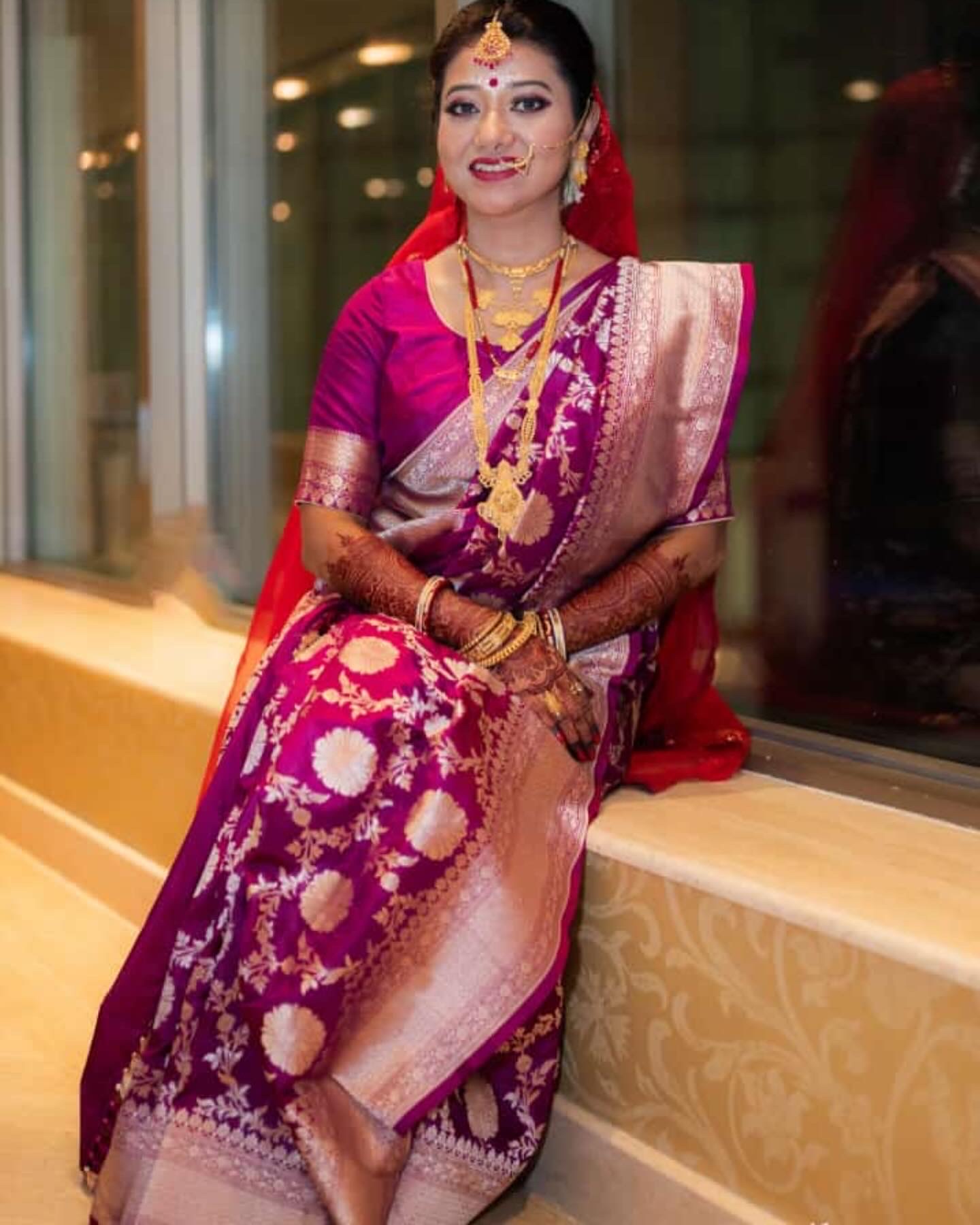 Seated bride in a violet silk saree with traditional jewellery and makeup