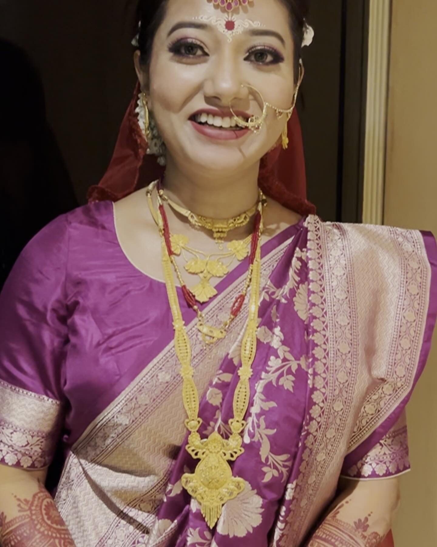 Smiling Bengali bride in a violet saree with traditional bridal makeup